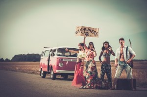 Multi-ethnic hippie hitchhikers with guitar and luggage on a road